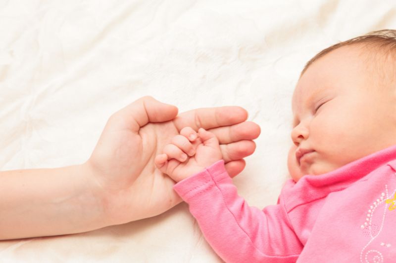 Schlafendes Baby, seine Hand liegt auf der Hand der Mutter.