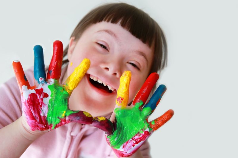 Kind mit Downsyndrom mit farbig bemalten Händen