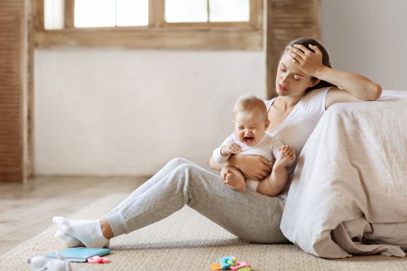 Mutter mit Baby, sitzend auf dem Boden Mutter hält sich sitzend auf dem Boden den Kopf, ihr Baby weint
